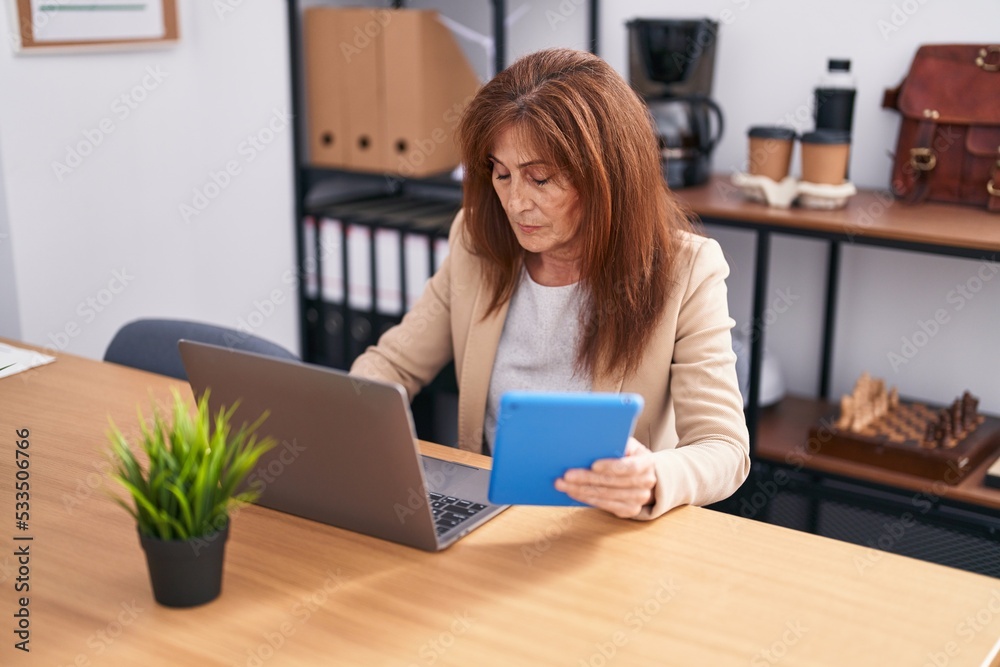 Middle age woman business worker using laptop and touchpad working at office Middle age woman business worker using laptop and touchpad working at office