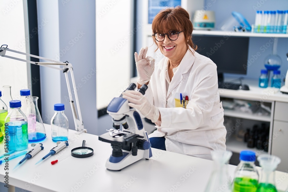 Middle age hispanic woman working at scientist laboratory doing ok sign with fingers, smiling friendly gesturing excellent symbol Middle age hispanic woman working at scientist laboratory doing ok sign with fingers, smiling friendly gesturing excellent symbol