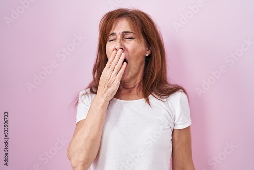 Schilderij op canvas Middle age woman standing over pink background bored yawning tired covering mouth with hand