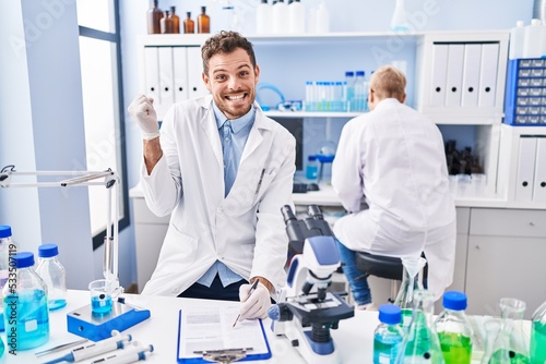 Hispanic man and woman working at scientist laboratory screaming proud  celebrating victory and success very excited with raised arm