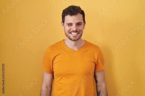 Wallpaper Mural Young hispanic man standing over yellow background winking looking at the camera with sexy expression, cheerful and happy face. Torontodigital.ca