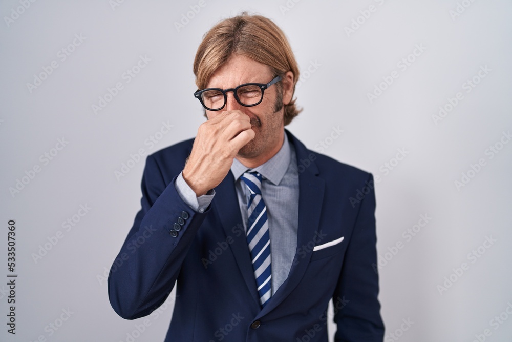 Caucasian man with mustache wearing business clothes smelling something stinky and disgusting, intolerable smell, holding breath with fingers on nose. bad smell Caucasian man with mustache wearing business clothes smelling something stinky and disgusting, intolerable smell, holding breath with fingers on nose. bad smell