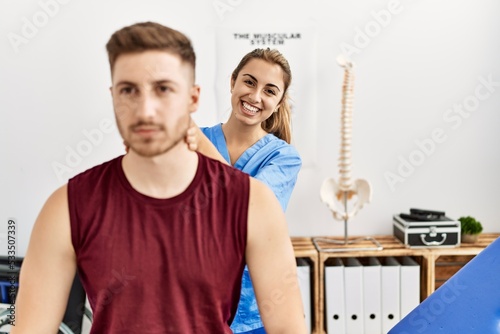 Young hispanic physioterapist woman make neck rehab treatment to man at the clinic. photo