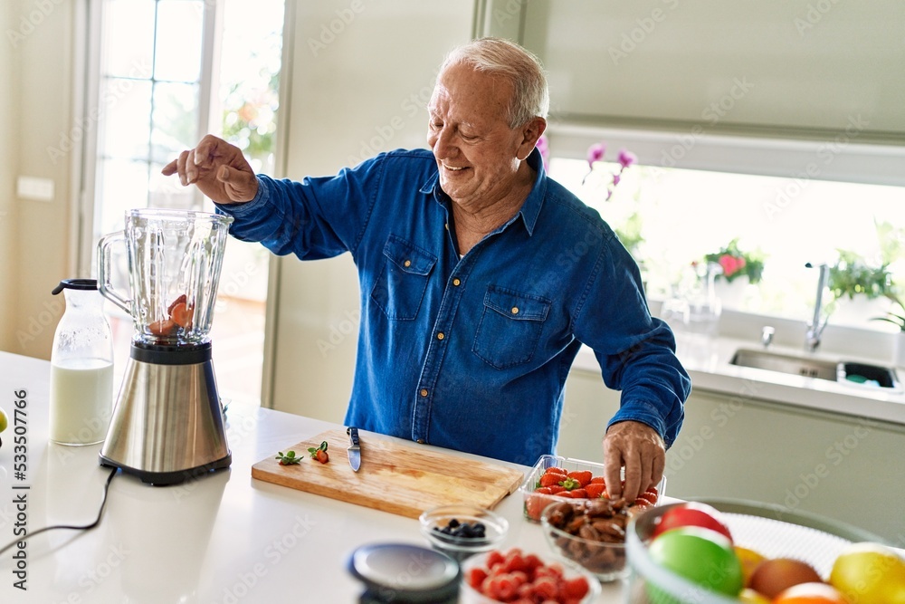 Senior man smiling confident putting strawberry in blender at kitchen