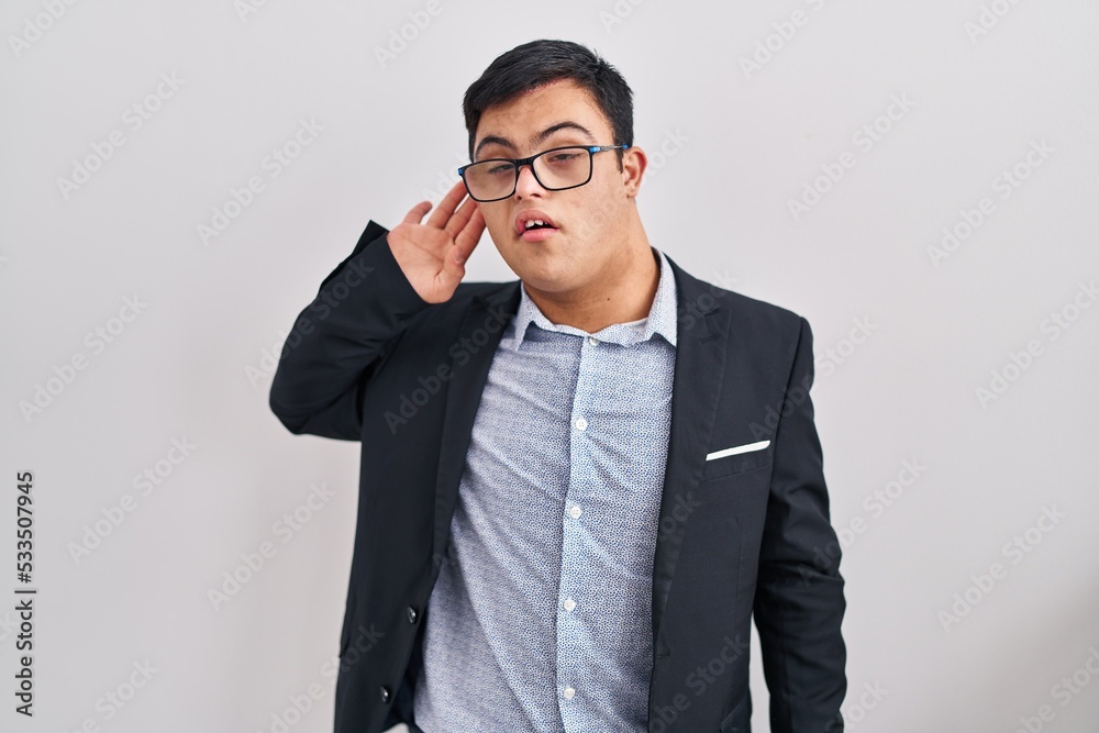 Young hispanic man with down syndrome wearing business style smiling with hand over ear listening an hearing to rumor or gossip. deafness concept. Young hispanic man with down syndrome wearing business style smiling with hand over ear listening an hearing to rumor or gossip. deafness concept.