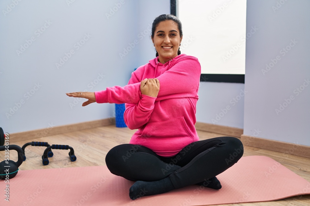 Young hispanic woman smiling confident stretching at sport center