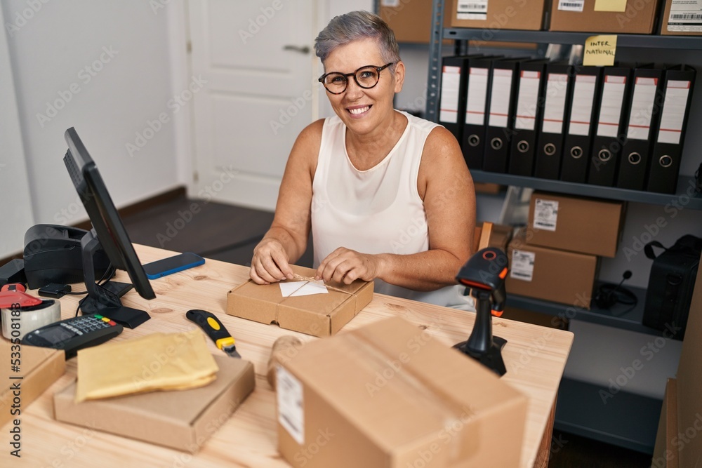 Middle age woman ecommerce business worker preparing package at office Middle age woman ecommerce business worker preparing package at office