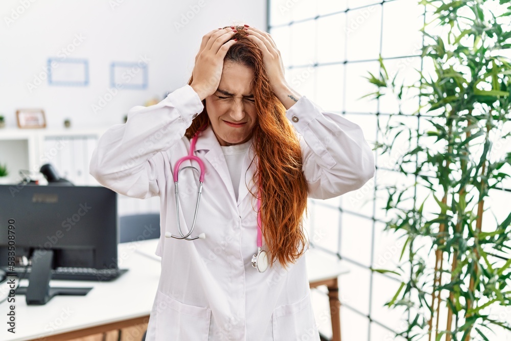 Young redhead woman wearing doctor uniform and stethoscope at the clinic suffering from headache desperate and stressed because pain and migraine. hands on head. Young redhead woman wearing doctor uniform and stethoscope at the clinic suffering from headache desperate and stressed because pain and migraine. hands on head.