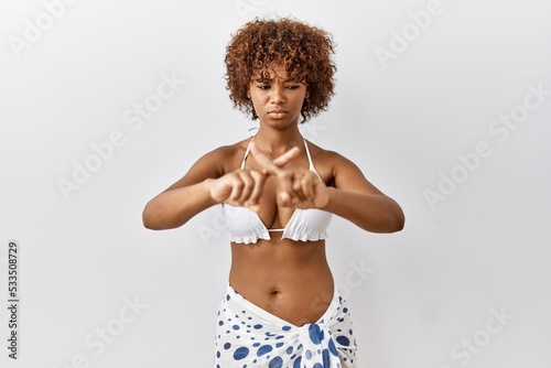 Young african american woman with curly hair wearing bikini rejection expression crossing fingers doing negative sign