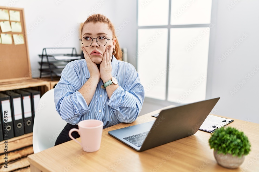 Young redhead woman working at the office using computer laptop tired hands covering face, depression and sadness, upset and irritated for problem Young redhead woman working at the office using computer laptop tired hands covering face, depression and sadness, upset and irritated for problem