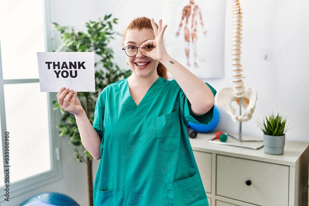 Young redhead physiotherapist woman working at pain recovery clinic holding thank you banner smiling happy doing ok sign with hand on eye looking through fingers Young redhead physiotherapist woman working at pain recovery clinic holding thank you banner smiling happy doing ok sign with hand on eye looking through fingers