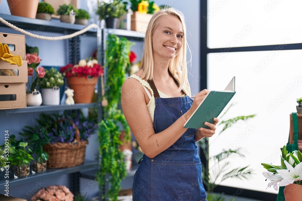 Young blonde woman florist smiling confident writing on book at florist store