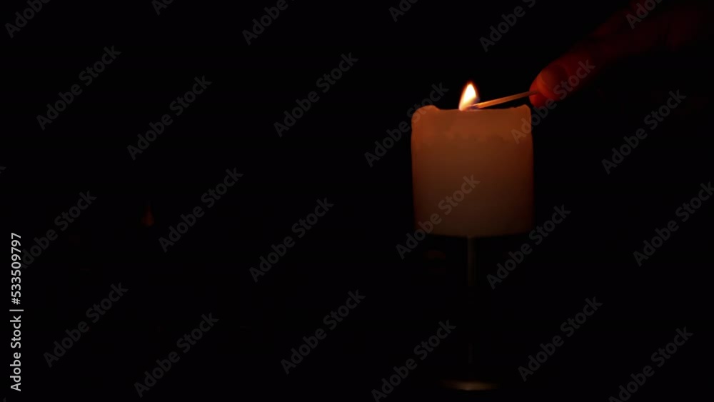 Hand Lights a Candle Wick in a Candlestick using a Match on a Black