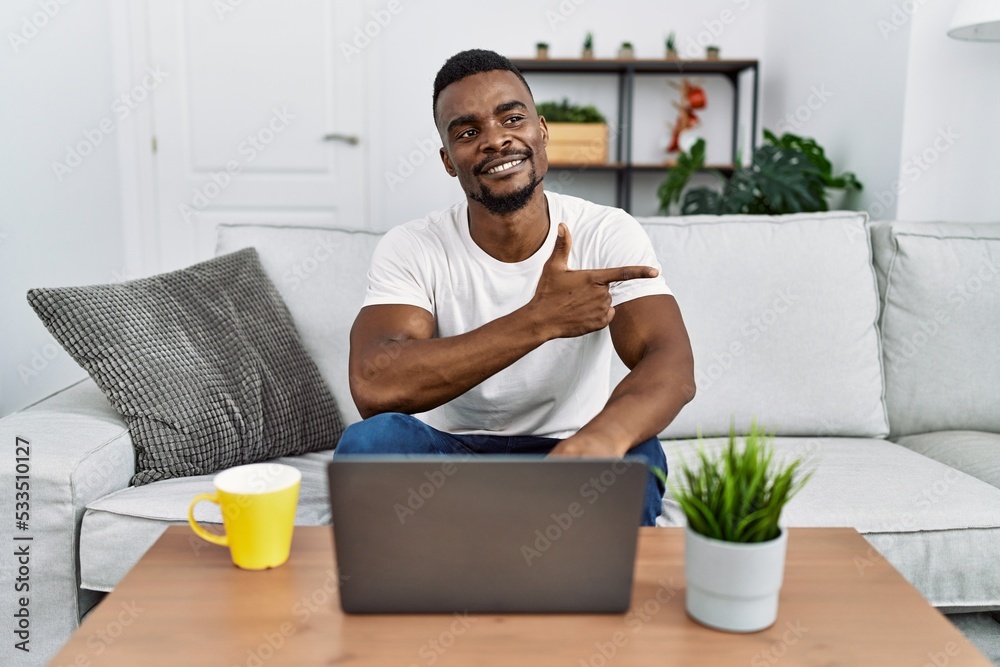 Young african man using laptop at home cheerful with a smile of face pointing with hand and finger up to the side with happy and natural expression on face