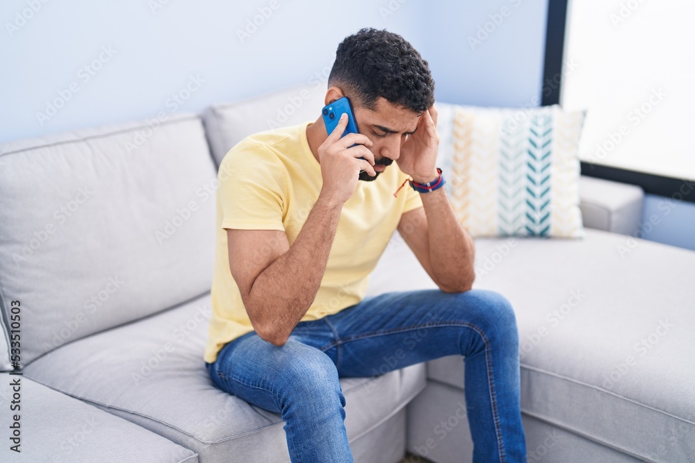 Young arab man talking on smartphone with worried expression at home Young arab man talking on smartphone with worried expression at home