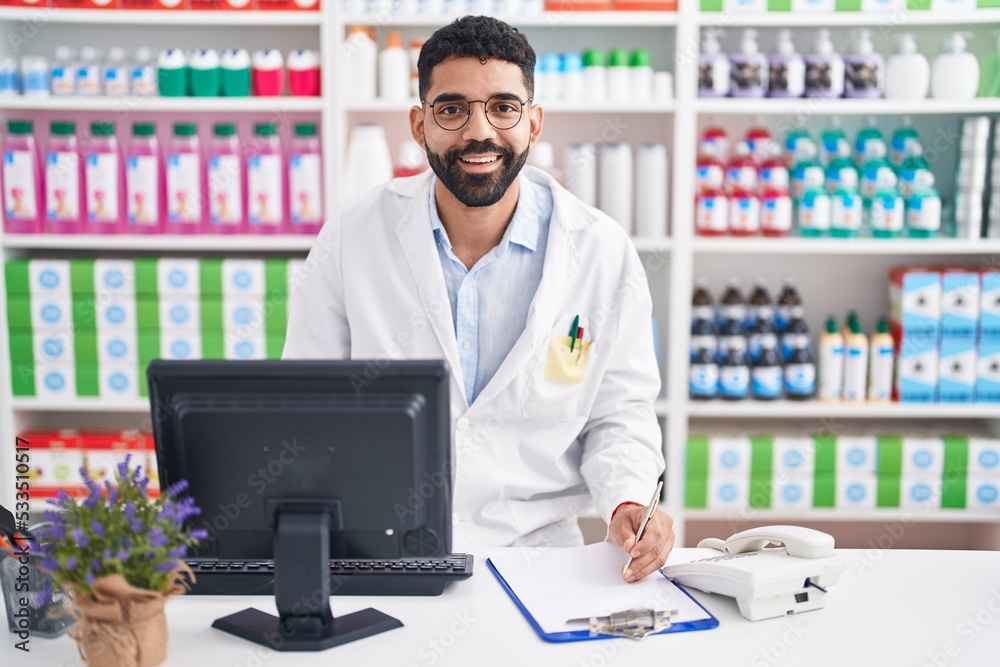 Young arab man pharmacist using computer writing on document at pharmacy