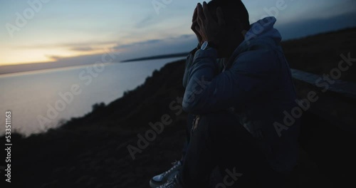 Alone depressed man sitting on the hill rubbing eyes
