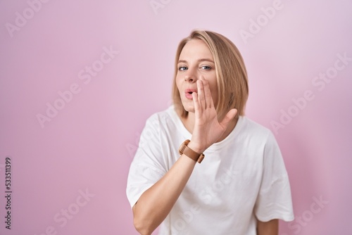 Young caucasian woman standing over pink background hand on mouth telling secret rumor, whispering malicious talk conversation