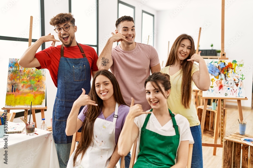 Group of five hispanic artists at art studio smiling doing phone gesture with hand and fingers like talking on the telephone. communicating concepts.