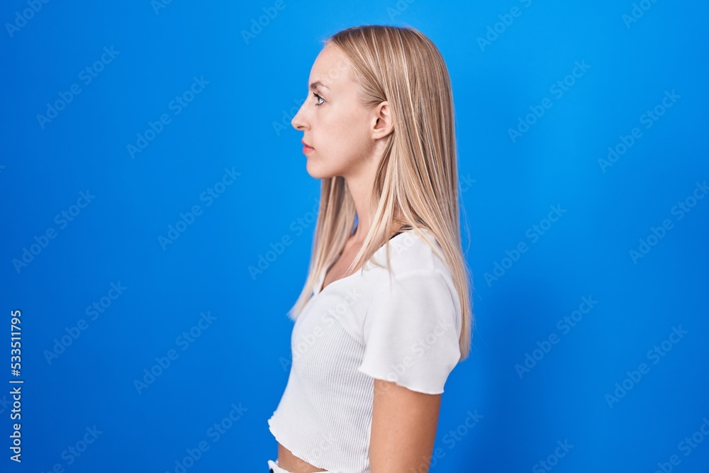 Young caucasian woman standing over blue background looking to side, relax profile pose with natural face and confident smile. Young caucasian woman standing over blue background looking to side, relax profile pose with natural face and confident smile.