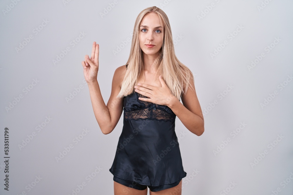 Young caucasian woman wearing nightgown smiling swearing with hand on chest and fingers up, making a loyalty promise oath Young caucasian woman wearing nightgown smiling swearing with hand on chest and fingers up, making a loyalty promise oath