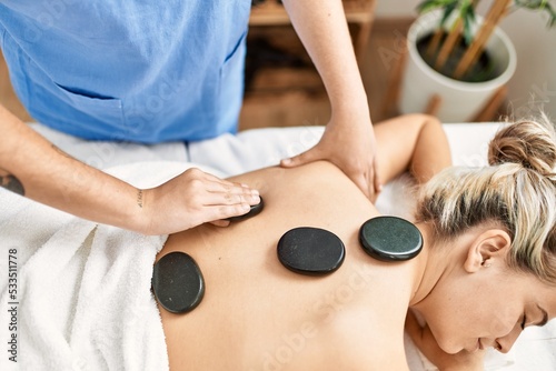 Woman couple having back treatment using hot black stones at beauty center photo