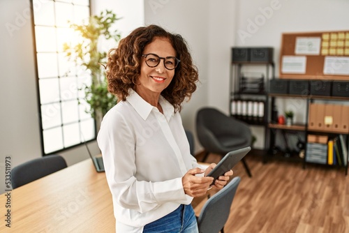 Middle age hispanic woman smiling confident working using touchpad at office