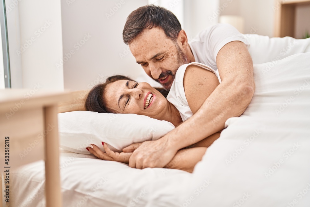Middle age man and woman couple hugging each other lying on bed at bedroom Middle age man and woman couple hugging each other lying on bed at bedroom
