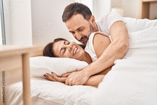 Middle age man and woman couple hugging each other lying on bed at bedroom