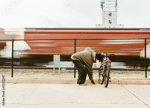 Homeless man with a bike collecting cans outdoors near the train tracks. Social problems of big modern cities.