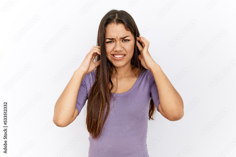 Young brunette woman standing by isolated background covering ears with fingers with annoyed expression for the noise of loud music. deaf concept. Young brunette woman standing by isolated background covering ears with fingers with annoyed expression for the noise of loud music. deaf concept.