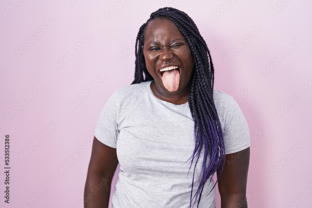 Young african woman standing over pink background sticking tongue out ...