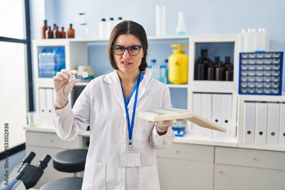 Young hispanic woman working at scientist laboratory with blood samples clueless and confused expression. doubt concept. Young hispanic woman working at scientist laboratory with blood samples clueless and confused expression. doubt concept.