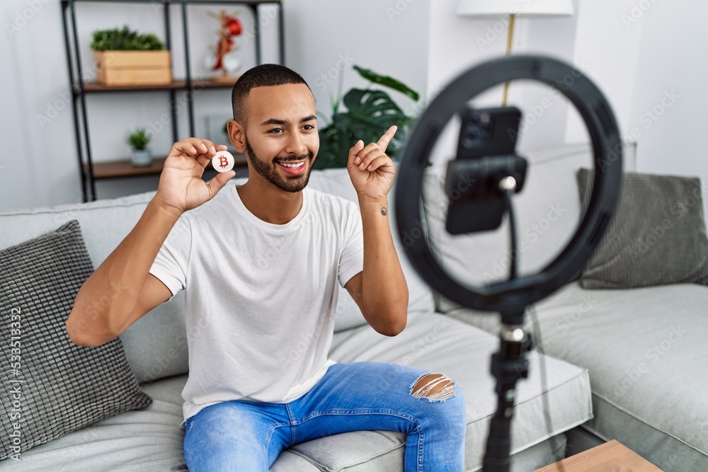 African american man recording vlog tutorial about bitcoin with smartphone at home smiling happy pointing with hand and finger to the side African american man recording vlog tutorial about bitcoin with smartphone at home smiling happy pointing with hand and finger to the side