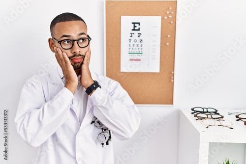 African american optician man standing by eyesight test tired hands covering face, depression and sadness, upset and irritated for problem