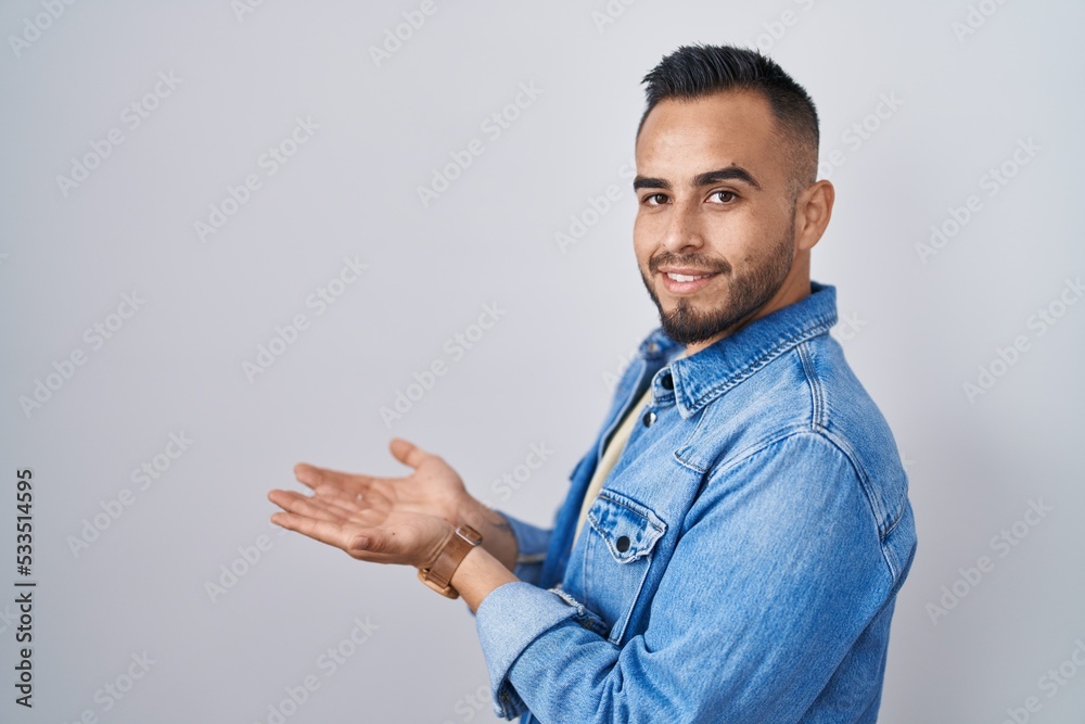 Fototapeta premium Young hispanic man standing over isolated background pointing aside with hands open palms showing copy space, presenting advertisement smiling excited happy