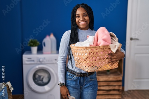 African american woman holding laundry basket looking positive and happy standing and smiling with a confident smile showing teeth