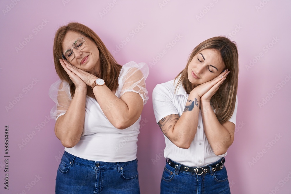 Hispanic mother and daughter wearing casual white t shirt over pink background sleeping tired dreaming and posing with hands together while smiling with closed eyes. Hispanic mother and daughter wearing casual white t shirt over pink background sleeping tired dreaming and posing with hands together while smiling with closed eyes.