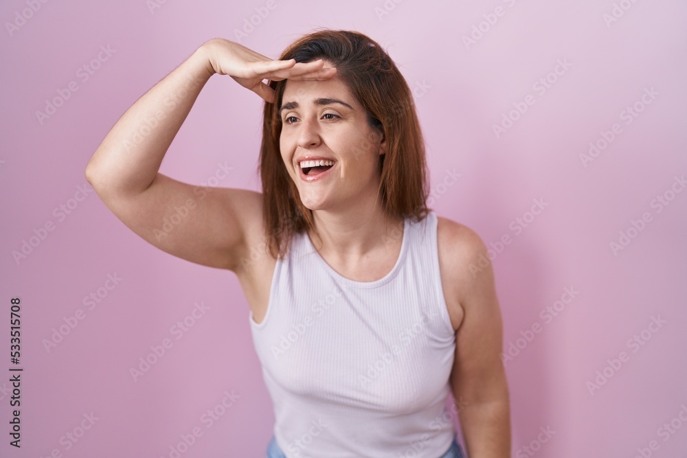 Brunette woman standing over pink background very happy and smiling looking far away with hand over head. searching concept. Brunette woman standing over pink background very happy and smiling looking far away with hand over head. searching concept.