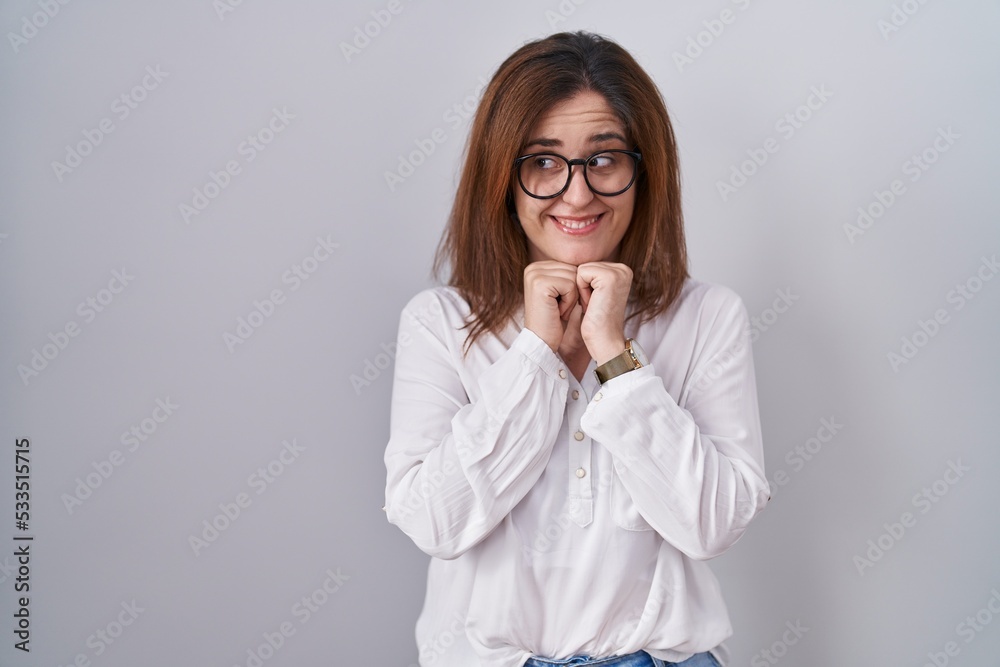 Brunette woman standing over white isolated background laughing nervous and excited with hands on chin looking to the side Brunette woman standing over white isolated background laughing nervous and excited with hands on chin looking to the side