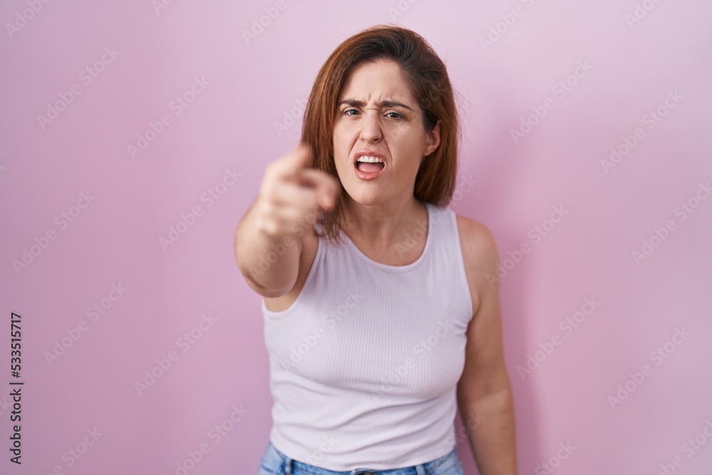 Brunette woman standing over pink background pointing displeased and frustrated to the camera, angry and furious with you Brunette woman standing over pink background pointing displeased and frustrated to the camera, angry and furious with you