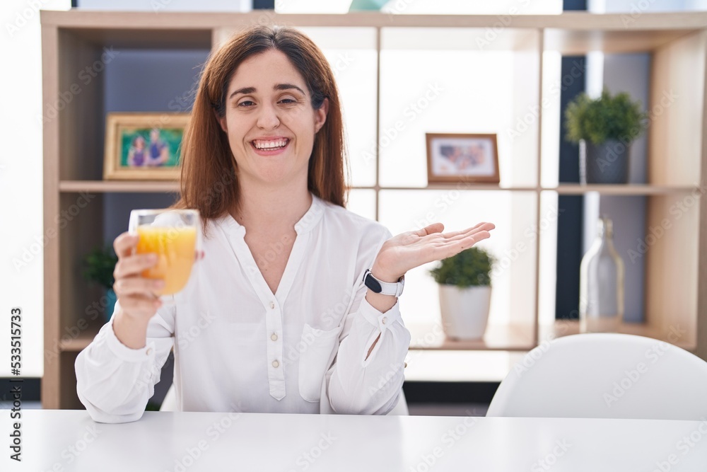 Brunette woman drinking glass of orange juice pointing aside with hands open palms showing copy space, presenting advertisement smiling excited happy Brunette woman drinking glass of orange juice pointing aside with hands open palms showing copy space, presenting advertisement smiling excited happy