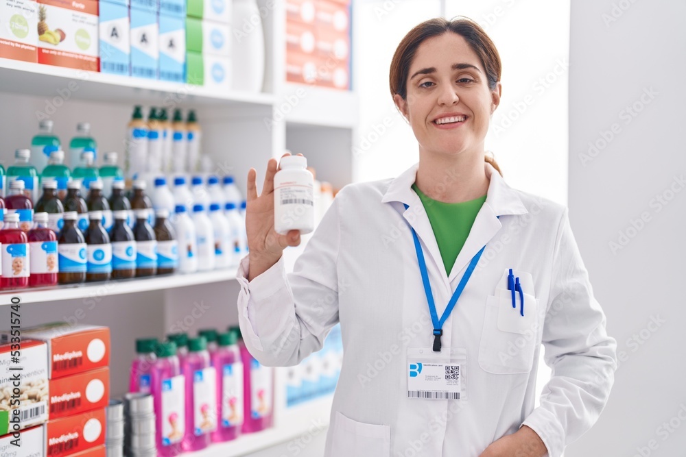 Young woman pharmacist smiling confident holding pills bottle at pharmacy Young woman pharmacist smiling confident holding pills bottle at pharmacy