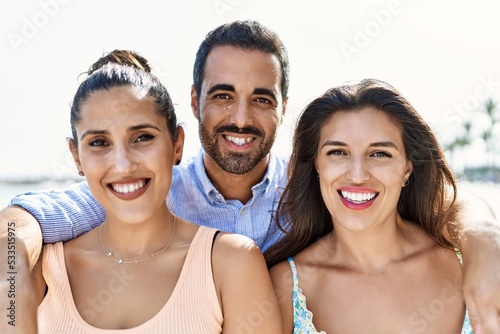 Three young hispanic friends smiling happy and hugging at the beach.