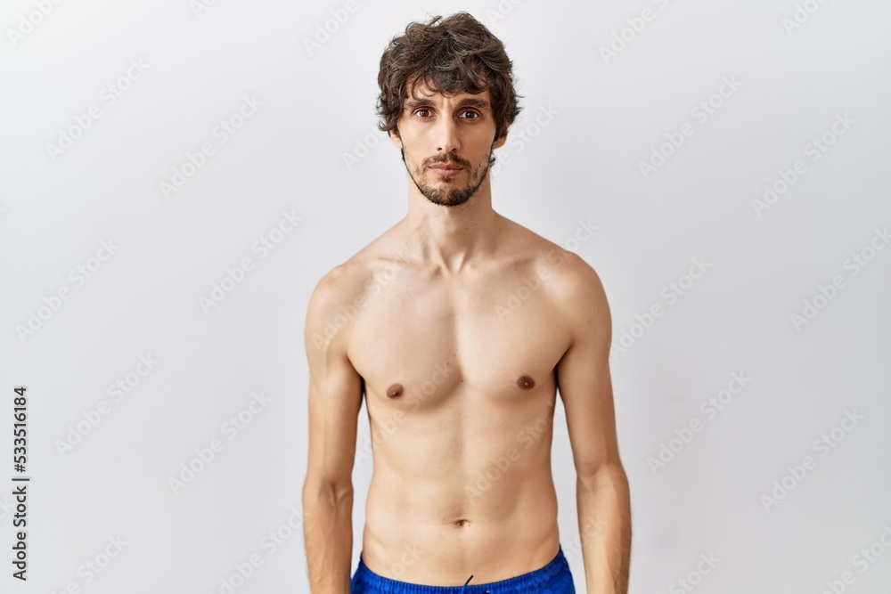 Young hispanic man standing shirtless over isolated, background relaxed with serious expression on face. simple and natural looking at the camera.