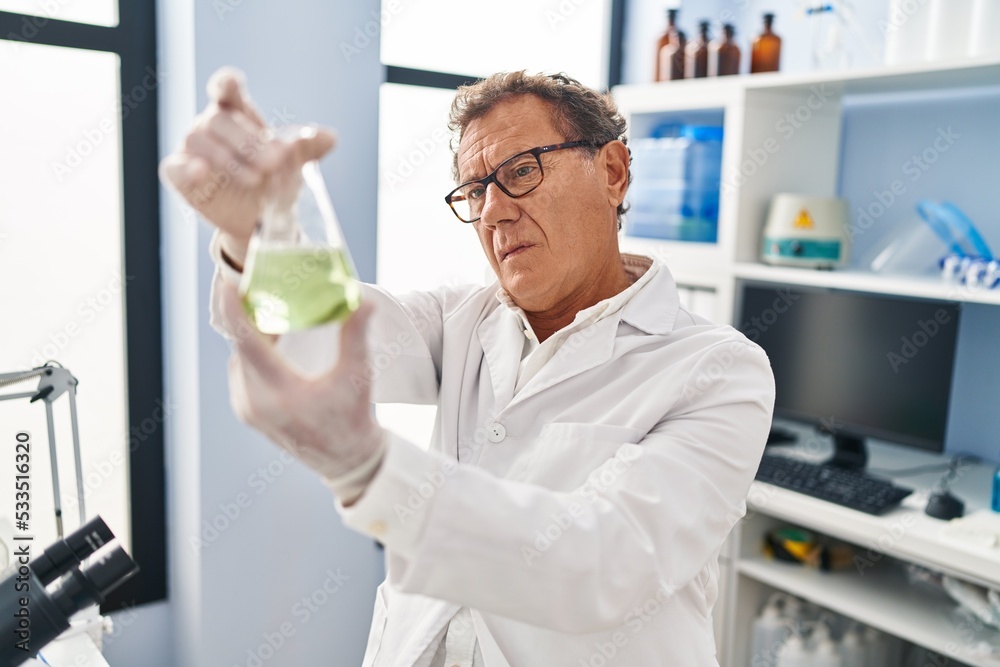 Middle age man wearing scientist uniform looking test tube at laboratory