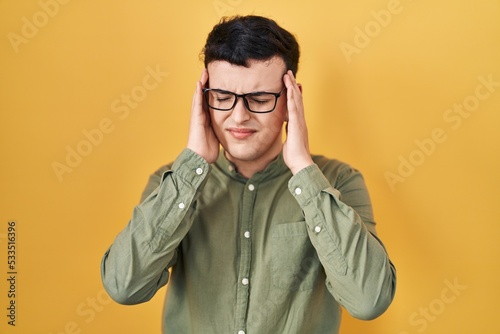 Non binary person standing over yellow background with hand on head for pain in head because stress. suffering migraine.