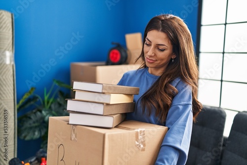 Young hispanic woman smiling confident holding books package at new home