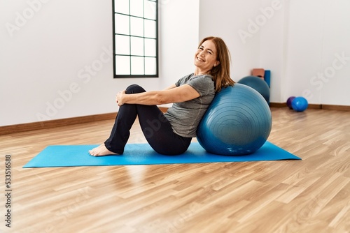 Middle age caucasian woman smiling confident training using fit ball at sport center