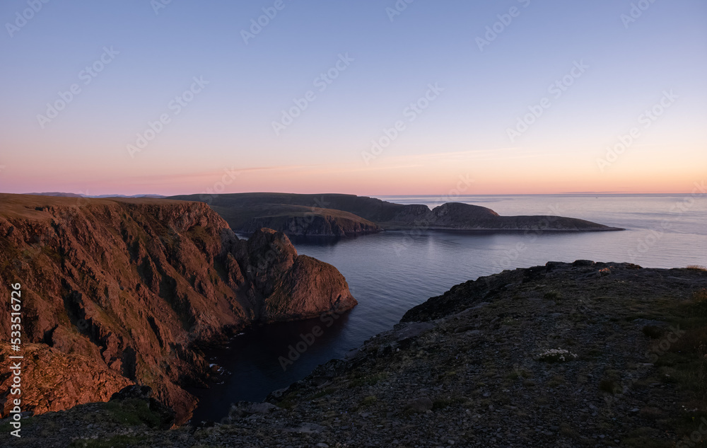 Wonderful landscapes in Norway. Nord-Norge. Beautiful scenery of a midnight sun sunset at Nordkapp (Cape North). Boat and globe on a cliff. Rippled sea and clear orange sky. Selective focus